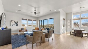 A spacious living room with a large window, a ceiling fan, and a dining area with a table and chairs. - Villa #02 at Bloomington Country Club: Pool, Golf, Restaurant (St. George)