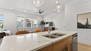 Une cuisine moderne dotée d’un grand îlot central, d’appareils électroménagers en acier inoxydable et de luminaires suspendus.