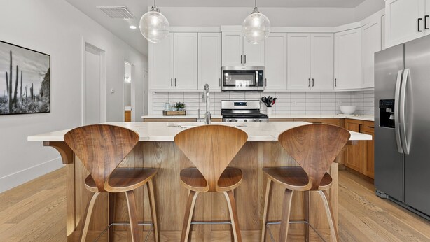 Une cuisine moderne avec des meubles blancs, des appareils en acier inoxydable et des tabourets de bar en bois.