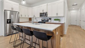 A modern kitchen with white cabinets, stainless steel appliances, a central island with bar stools, and pendant lighting. - Villa #36 at Bloomington Country Club: Pool, Golf, Restaurant (St. George)