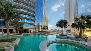 Un hôtel moderne doté d’une grande piscine extérieure, de palmiers et, en arrière-plan, d’immeubles de grande hauteur.