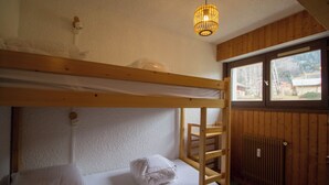 Une chambre avec un lit superposé, une échelle en bois, un radiateur et une fenêtre donnant sur des immeubles et des arbres.