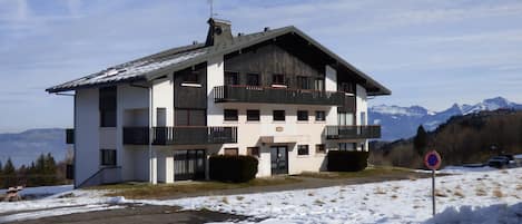 Un immeuble à plusieurs étages doté de balcons, une piste de ski en arrière-plan et de la neige au sol.