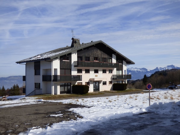 A multi-story building with balconies, a ski slope in the background, and snow on the ground.
