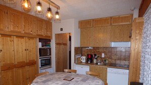 Une cuisine avec des meubles de rangement en bois, une table à manger avec des chaises, un four à micro-ondes, une machine à café et un lave-vaisselle.
