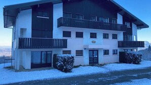 Un immeuble à plusieurs étages doté de balcons, d’une entrée centrale et d’un sol recouvert de neige.