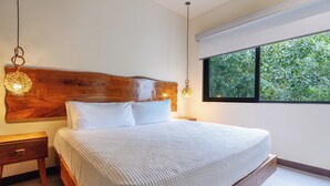 A bedroom with a wooden headboard, a large window with a view of greenery, and a bedside lamp. - Villa in Tulum with Private Pool and Jacuzzi (Tulum)
