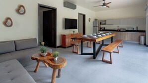 A modern living room with a grey sofa, wooden coffee table, and bench, a dining area with a wooden table and benches, and a kitchen in the background. - Villa in Tulum with Private Pool and Jacuzzi (Tulum)