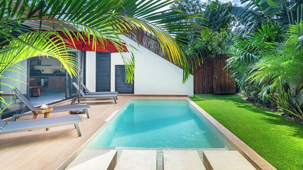 A modern outdoor pool area with lounge chairs, a wooden deck, and a well-maintained lawn. - Villa in Tulum with Private Pool and Jacuzzi (Tulum)
