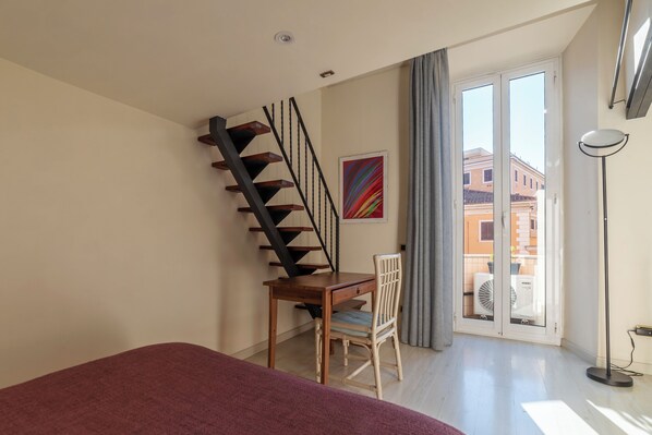 A bedroom with a bed, a desk, a chair, a staircase, and a view of the outside. - Casa Emma - Charme Holidays (Rome)