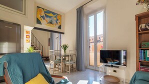 Un salon moderne comprenant un canapé, une table à manger, des chaises, un téléviseur posé sur un meuble et une vue sur l’extérieur grâce à une porte vitrée.