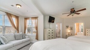 A bedroom with a bed, a sofa, a TV, a ceiling fan, and a dresser.