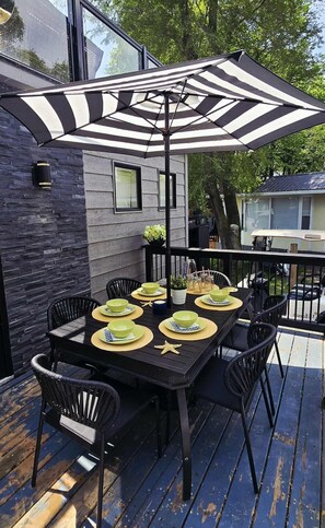 An outdoor dining area with a black table and chairs, a striped umbrella, and a stone wall backdrop. - Sherkston Rooftop Retreat (Port Colborne)