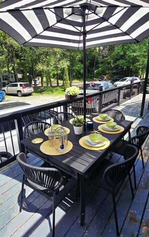 An outdoor patio with a black and white striped umbrella, black metal chairs, and a table set for dining with green plates and bowls. - Sherkston Rooftop Retreat (Port Colborne)