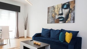 Un soggiorno moderno con un divano blu scuro, un tavolino da caffè con vasi decorativi e un grande quadro astratto appeso al muro.