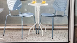 Un balcone con due sedie blu e un tavolino bianco, ognuna con una tazza gialla.