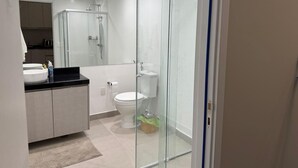 Un baño moderno con cabina de ducha de vidrio, inodoro blanco y lavamanos con encimera negra.