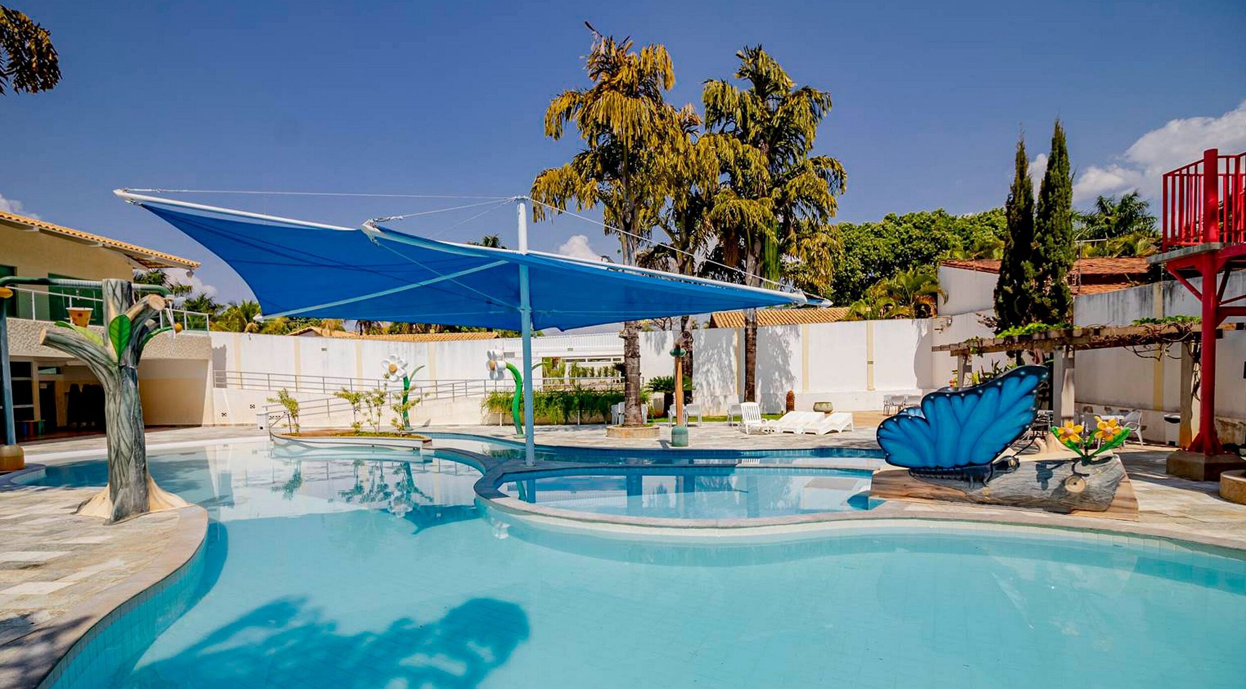 A swimming pool with a blue canopy, surrounded by palm trees and a red structure.