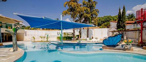 A swimming pool with a blue canopy, surrounded by palm trees and a red structure.