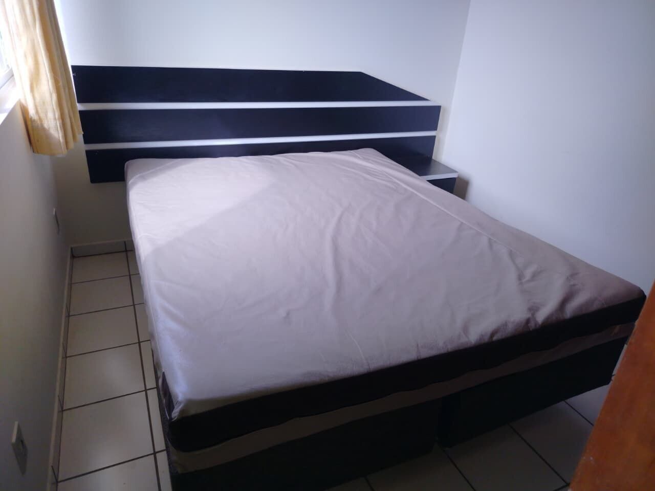 A single bed with a white mattress and a dark headboard in a small, tiled room.