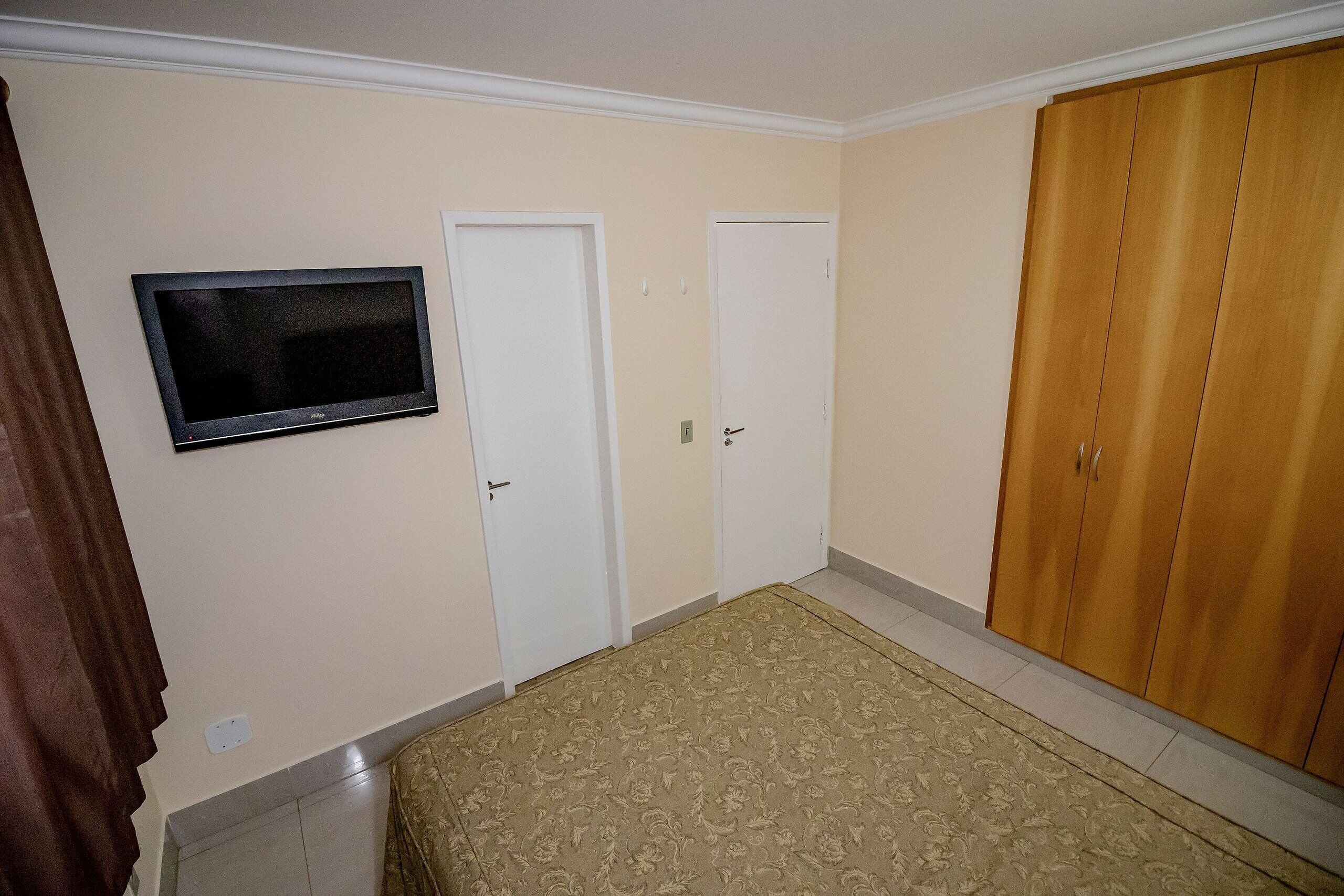 A bedroom with a bed, a television, two doors, and a wardrobe.