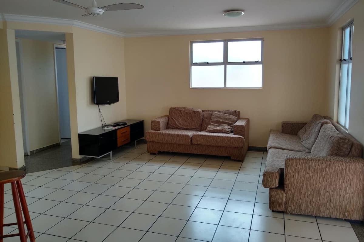 Ein Wohnzimmer mit einer Couch, einem Fernseher, einem Deckenventilator und einem großen Fenster.