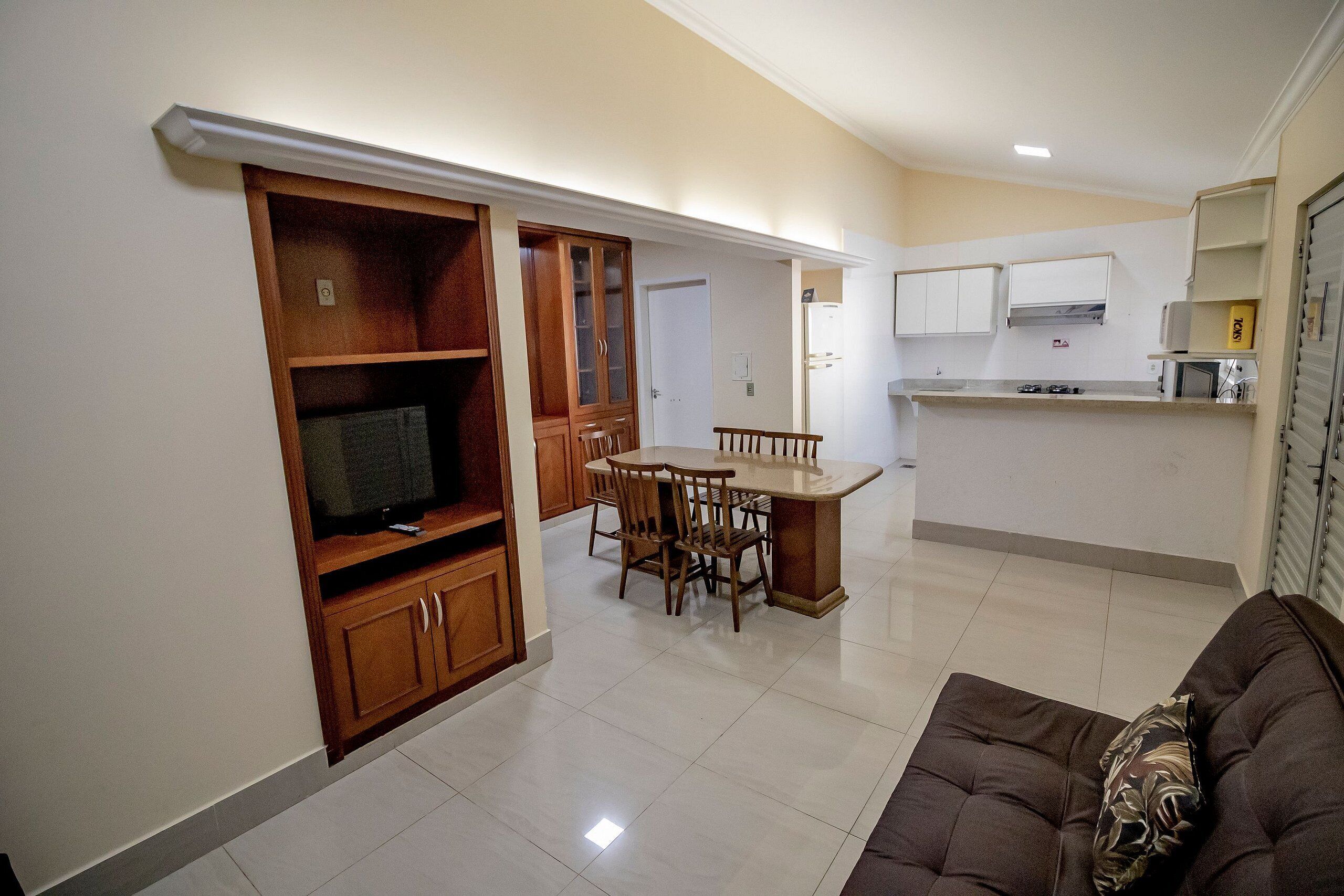 Una cocina moderna con armarios blancos, un comedor con mesa y sillas de madera, y una sala de estar con sofá marrón.