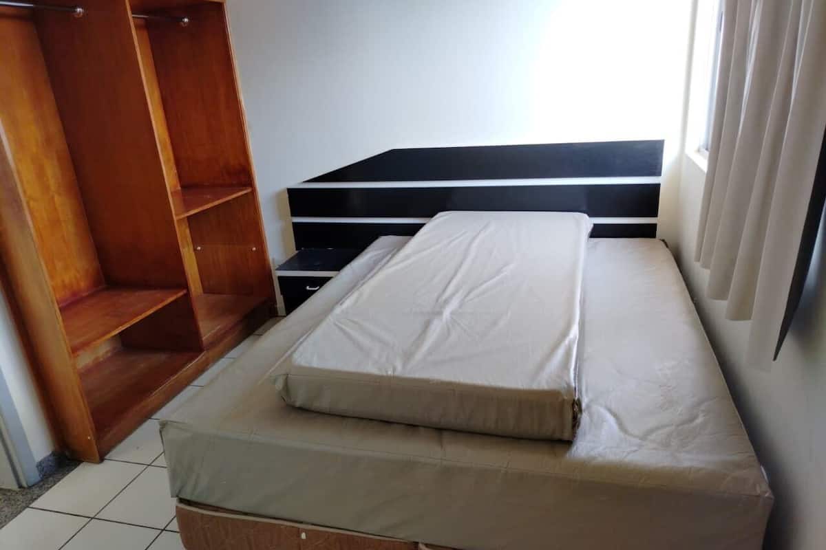 Ein Zimmer mit einem Bett, einem Holzschrank und einem Fenster mit Vorhängen.