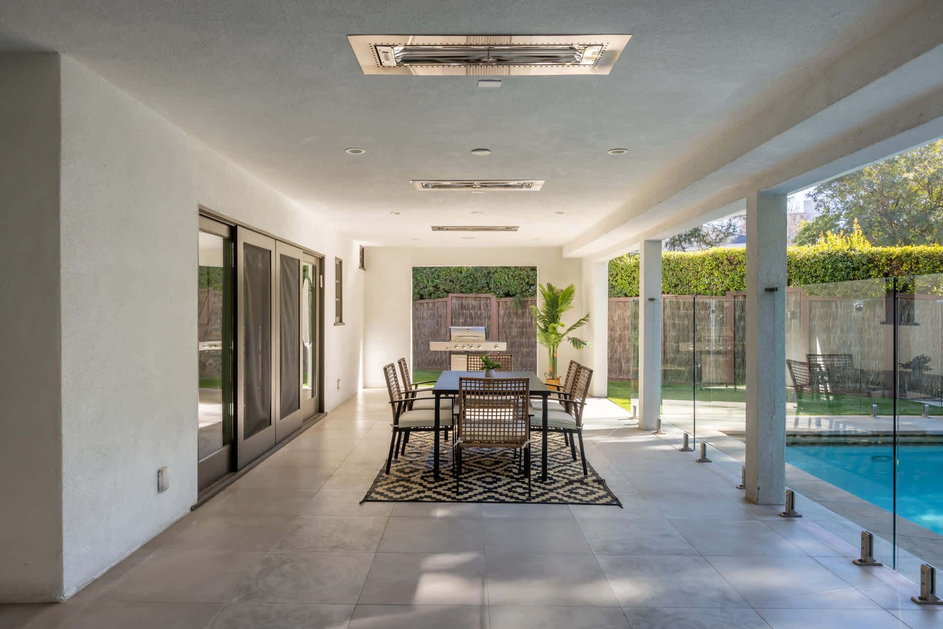 Un patio couvert avec une table et des chaises, un barbecue et une piscine.