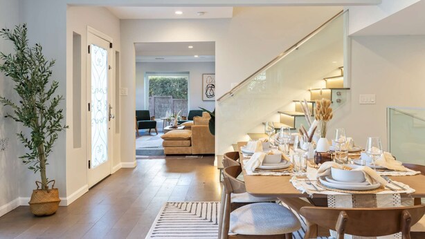 Un coin repas avec une table en bois dressée pour quatre personnes, une plante en pot et une vue sur un salon comprenant un canapé et une table à manger.