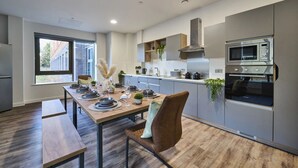 Une cuisine moderne avec des meubles gris, un four à micro-ondes encastré et un coin repas avec une table en bois, dressée pour quatre personnes.