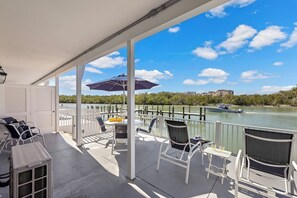 A covered outdoor area with white chairs, a table, and an umbrella. A boat is visible on the water in the background. - Coastal waterfront condo located in Olde Marco (Marco Island)