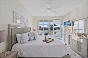 A hotel room with a bed, a dresser, a ceiling fan, a TV, and a window with a view of the outside. - Coastal waterfront condo located in Olde Marco (Marco Island)