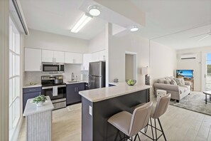 A modern kitchen with a central island, stainless steel appliances, and a dining area with bar stools. - Coastal waterfront condo located in Olde Marco (Marco Island)