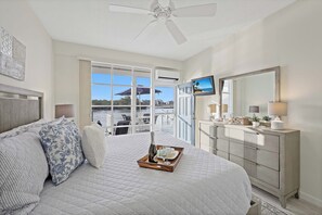 A bedroom with a bed, a dresser, a TV, and a balcony with a view of the water. - Coastal waterfront condo located in Olde Marco (Marco Island)