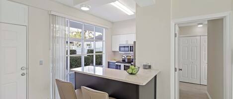 A modern kitchen with a central island, a dining area with two chairs, and a view through the window.