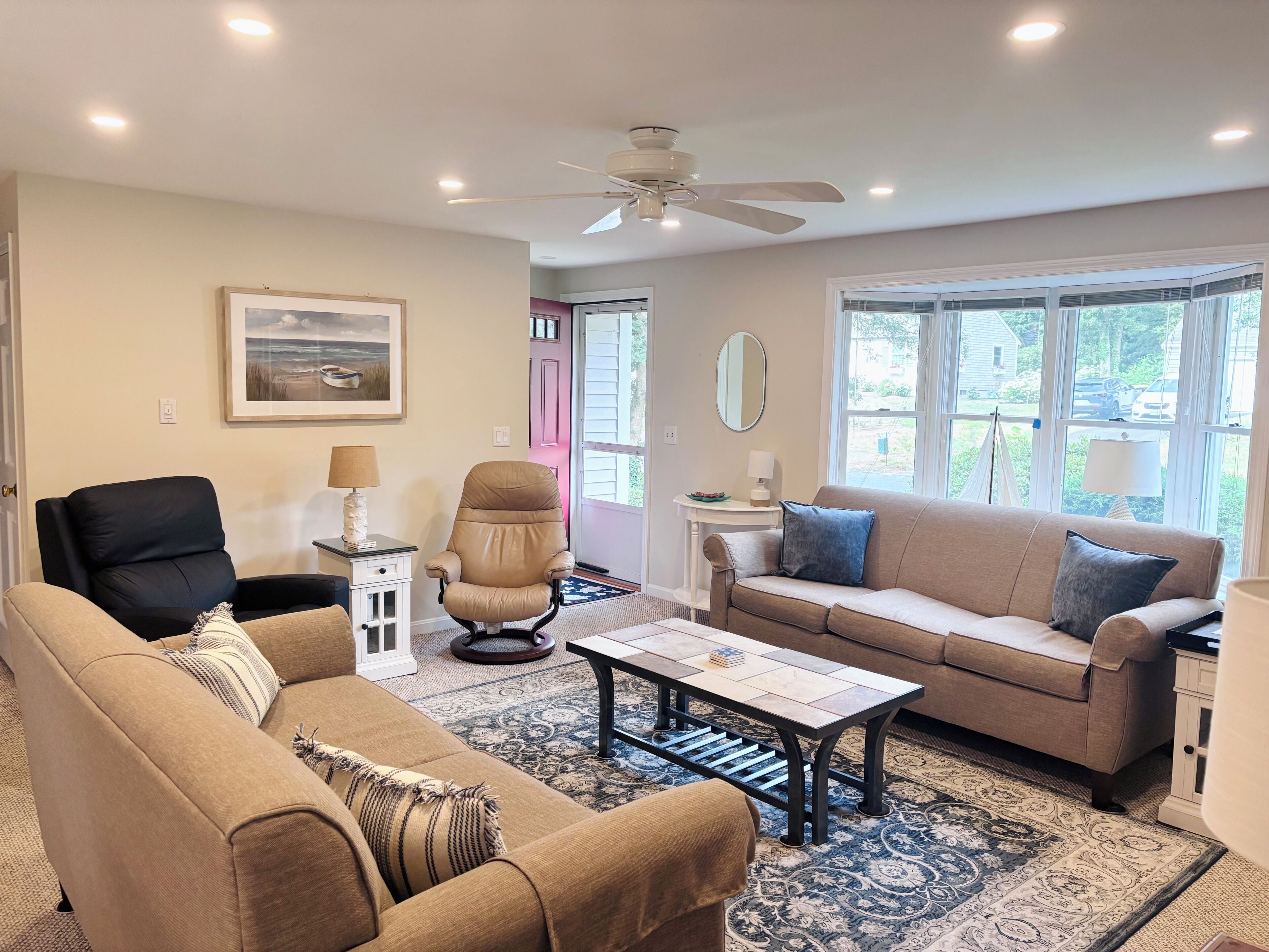 A living room with a beige sofa, a black chair, a coffee table, and a ceiling fan.