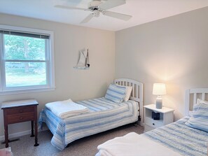 A bedroom with two beds, a ceiling fan, a nightstand with a lamp, and a window with blinds.