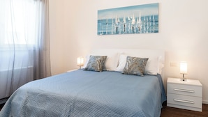 Une chambre à coucher avec un lit, deux tables de chevet, un tableau et une fenêtre avec des rideaux.