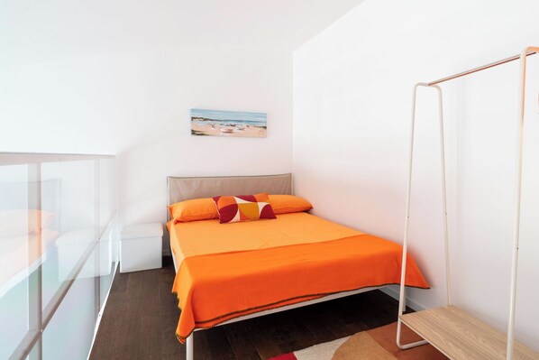 A bedroom with a bed, a small bedside table, a chair, a window with a view of the beach, and a painting on the wall. - Lolita's Beachfront Loft by Wonderful Italy (Bari)