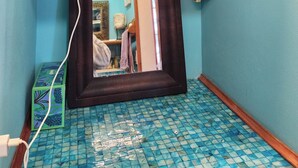 Un baño con piso de baldosas, un espejo y toallas sobre una repisa.