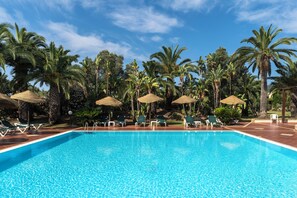 Una piscina con lettini e ombrelloni, circondata da palme.