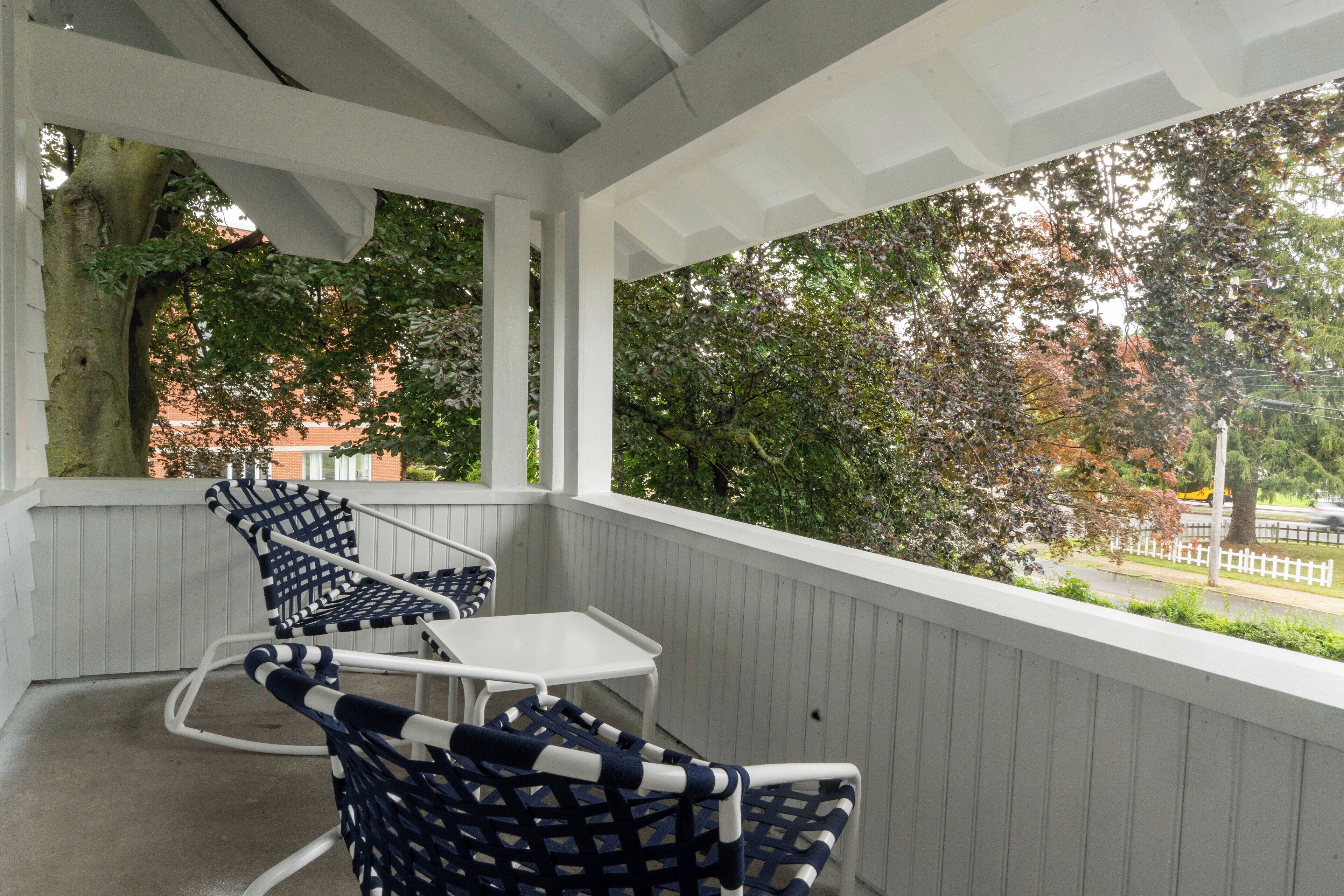 A covered porch with white railings, two wicker chairs, and a small table.