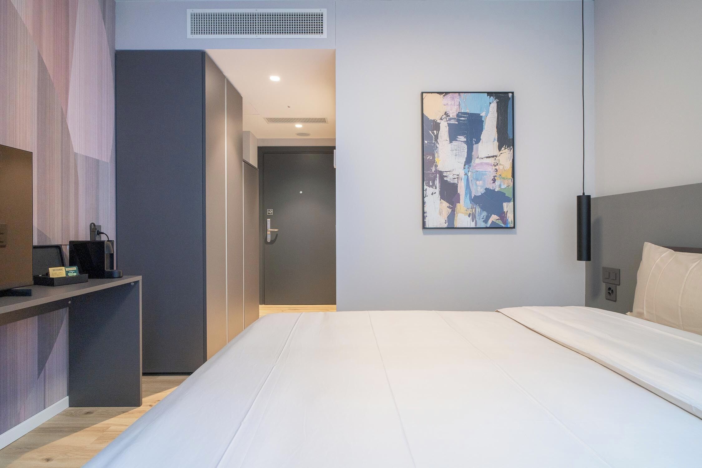 A modern hotel room with a large bed, a desk with a computer, and a painting on the wall.