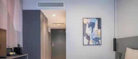 Una habitación de hotel moderna con una cama grande, un escritorio con computadora y un cuadro en la pared.