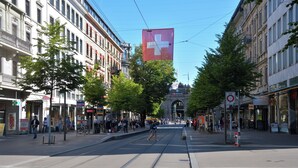 Een straat met tramrails, gebouwen en een grote Zwitserse vlag.