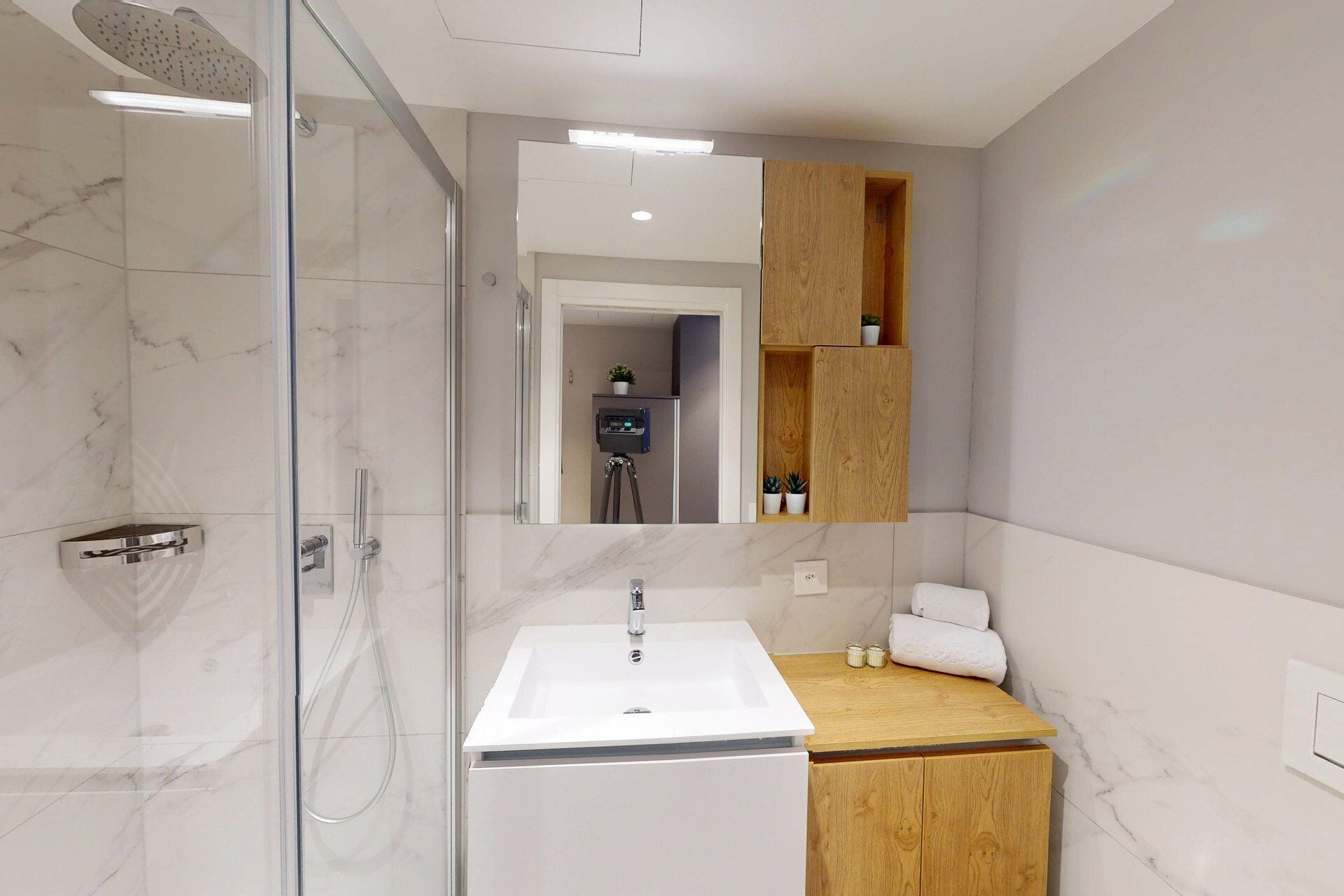 Un baño moderno con cabina de ducha de vidrio, un lavamanos blanco y muebles de madera.