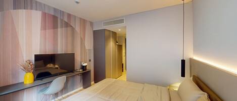 A modern hotel room with a bed, a desk with a chair, a TV, and a bedside table with a lamp.