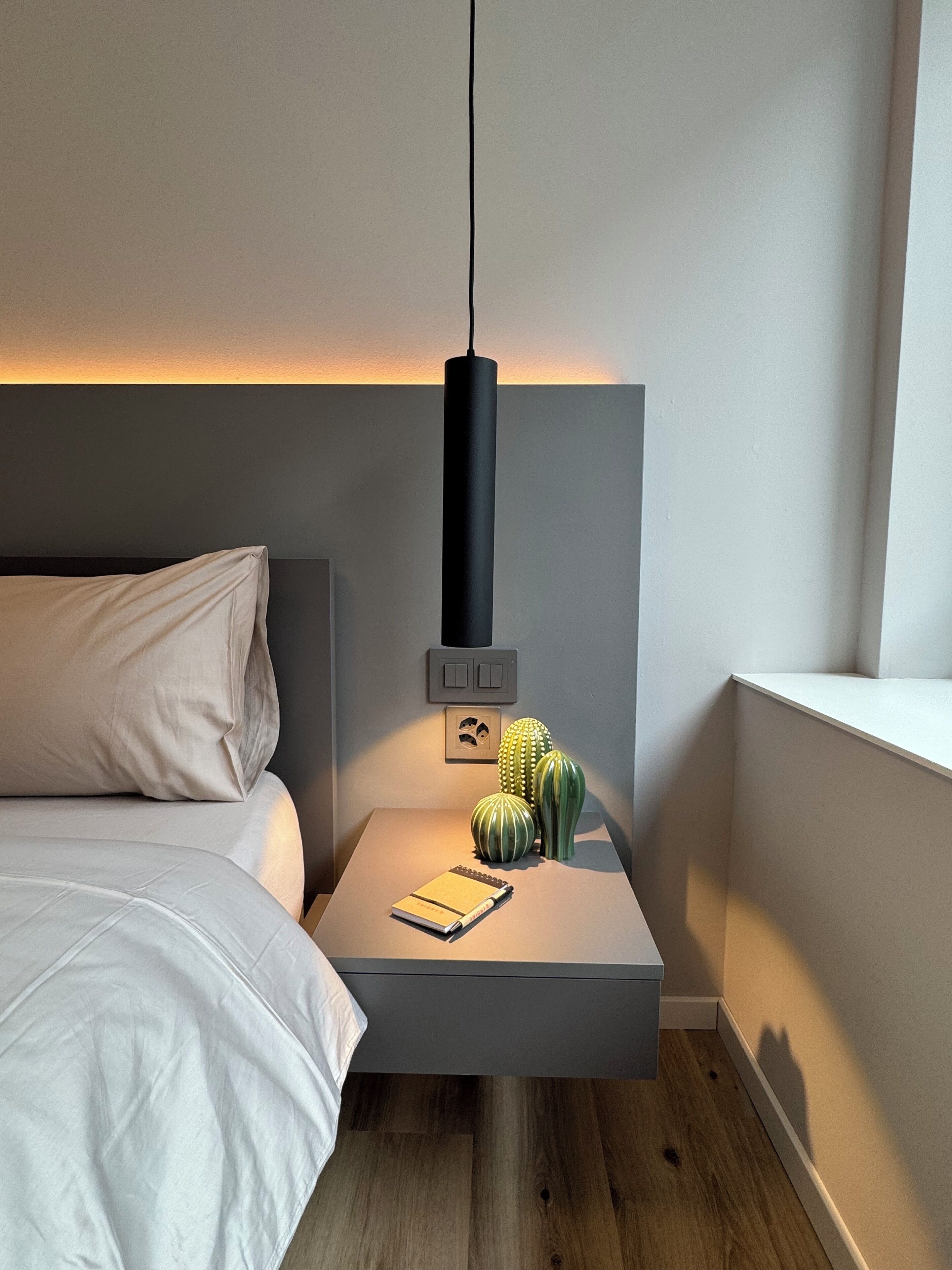 A modern bedroom with a bed, bedside table, and a hanging light fixture.