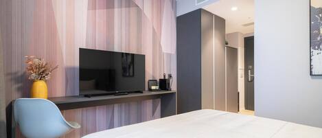 A modern hotel room with a bed, a TV on a stand, a desk with a chair, and a wall with a striped pattern.